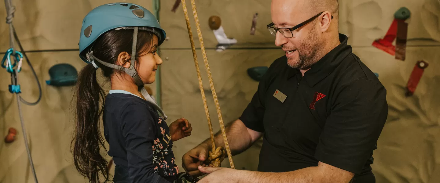 YMCA staff putting on climbing wall safety harness and equipment on youth