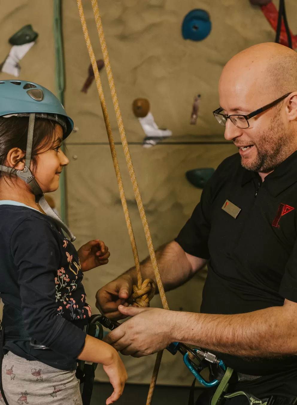 YMCA staff putting on climbing wall safety harness and equipment on youth