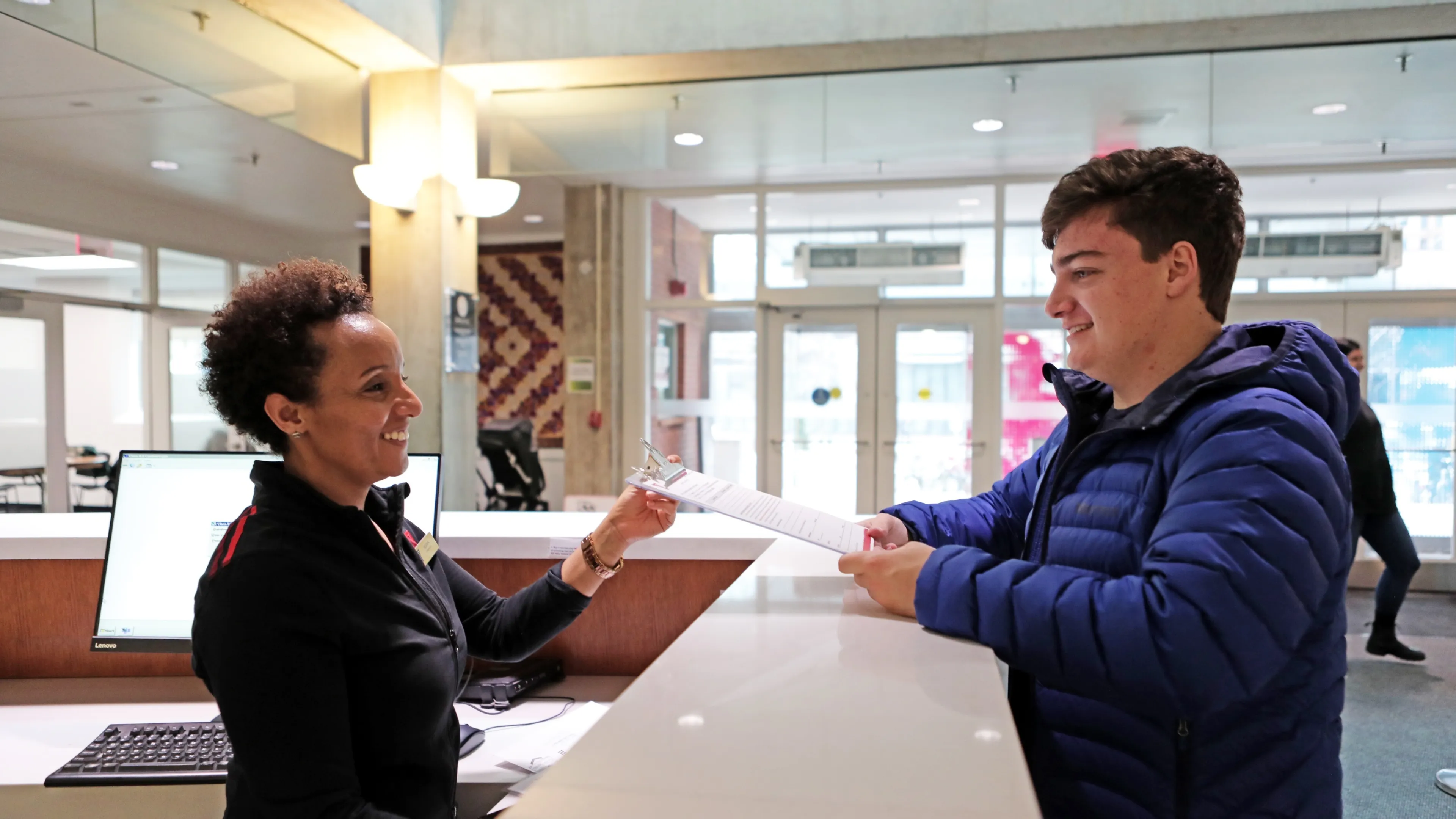 A photo of a young man handing a form to a YMCA employee at the front desk.