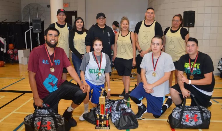 A group of youth pose for a photo amongst trophies at the 15th Annual Indigenous Hoops Tournament at YMCA Calgary in 2018