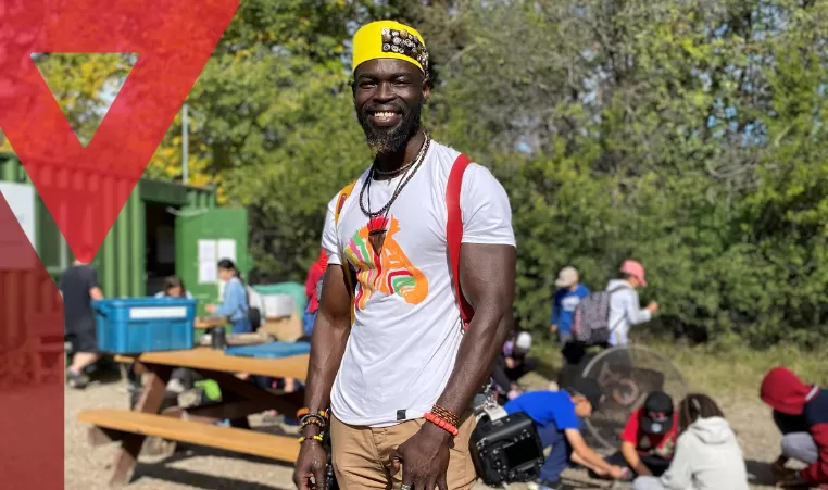 Sam Obadero stands in the sun at Camp Riveredge YMCA, smiling and donning his camera, which he can often be seen with accompanying the smile on his face.