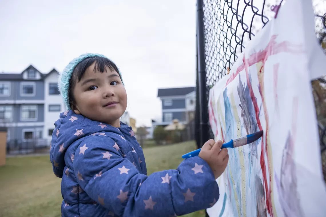 child standing in front of fence painting